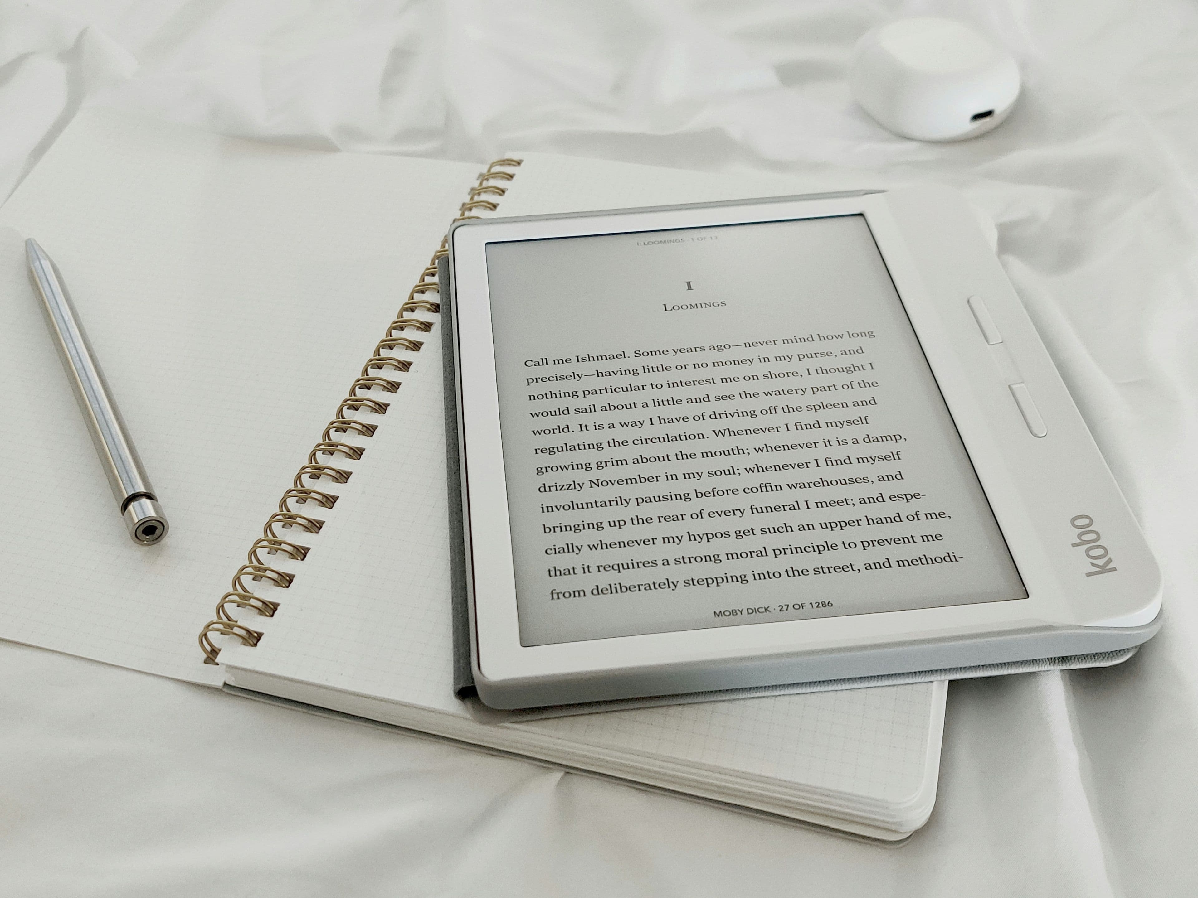 An e-reader resting on a table next to a paperback book